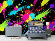 A colorful neon paint splatter wall mural displayed behind a gray bed, dresser, and nightstand in a modern bedroom setting.