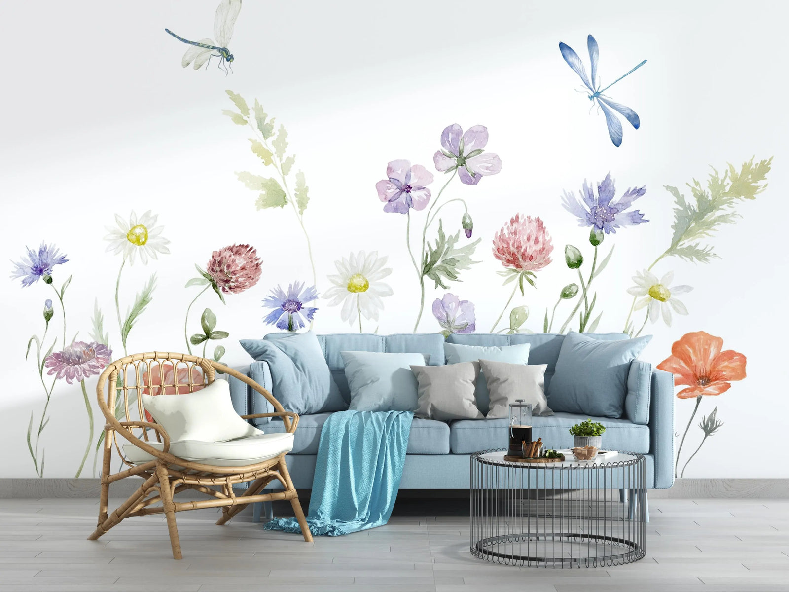 Living room with a light blue sofa, decorative pillows, a wicker chair, and a coffee table with a floral wall mural.