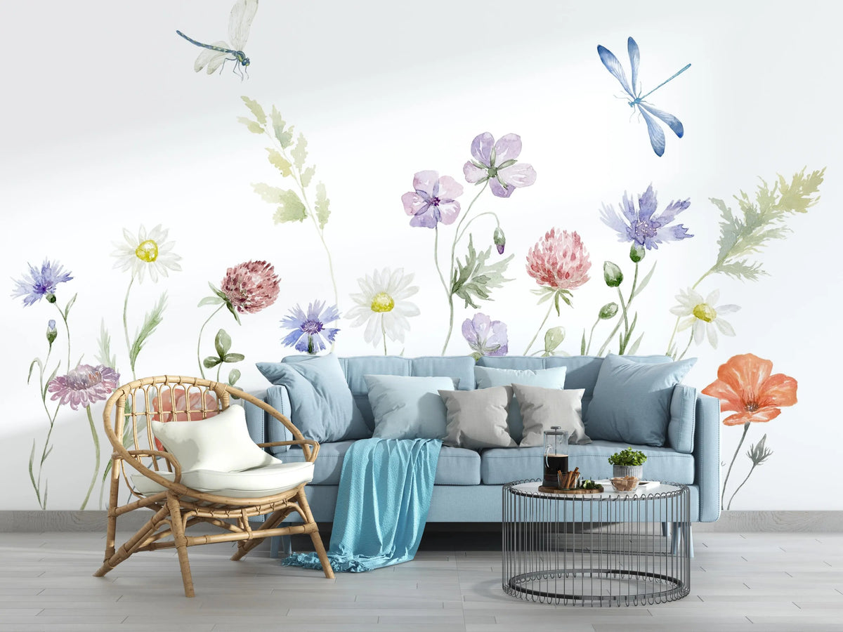 Living room with a light blue sofa, decorative pillows, a wicker chair, and a coffee table with a floral wall mural.