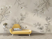 A styled interior scene showing a yellow armchair with gray pillows against a beige wall decorated with large gray botanical line drawings. A small wire side table with flowers sits to the left.
