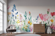 A colorful watercolor floral wall mural displayed on a wall in a styled room, featuring a gray armchair, a wooden dresser, and a plush toy.