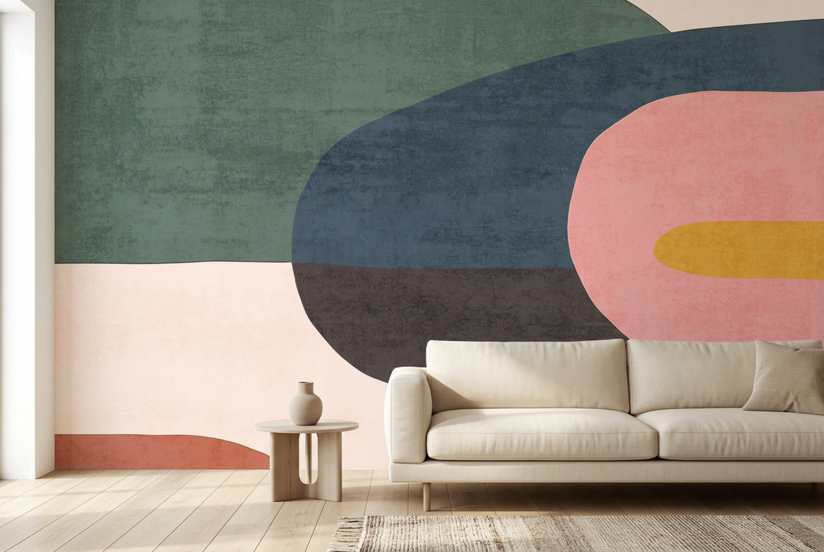 Abstract geometric wall mural with large organic shapes in muted green, navy, pink, charcoal, and mustard yellow, shown in a modern living room setting behind a cream sofa and small side table.