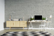 A modern home office setup featuring a textured gray wallpapered wall, a light wood sideboard, a white desk with a computer, lamp, and chair, and a black, white, and gray chevron rug on a light wood floor.