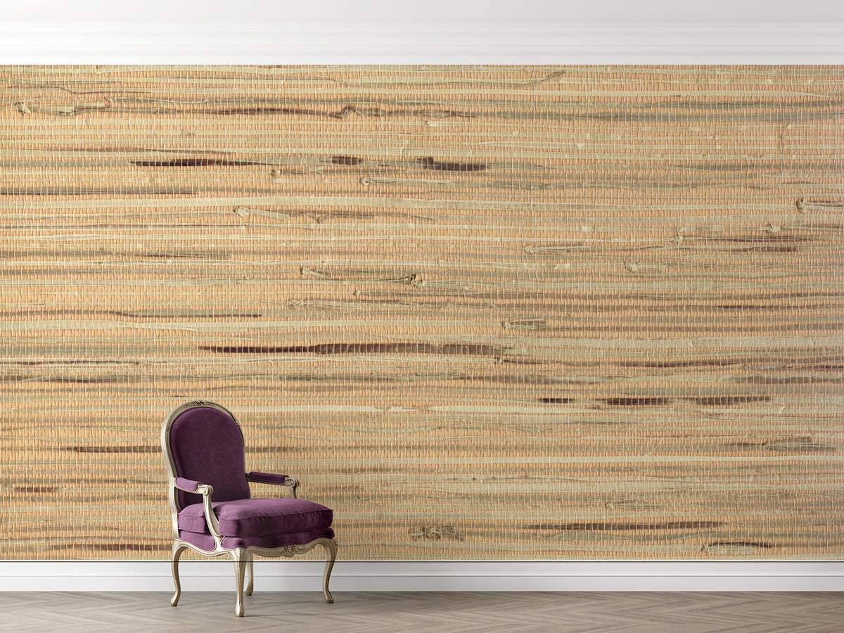 A large-scale woven wall mural with a natural jute or seagrass texture in warm beige and brown tones, shown in a room setting behind a purple velvet armchair.