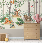 Woodland-themed wall mural featuring a bear cub, deer, squirrel, birds and lush green trees, decorating a cozy children's bedroom with a wooden house bed and natural decor.