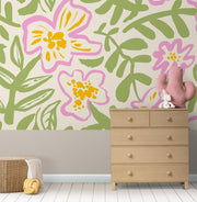 Floral wall mural with bold pink and yellow flowers and green leaves, decorating a nursery with a natural wood dresser, soft toys and a cozy basket.