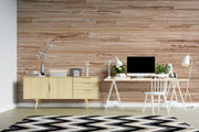 A modern home office setup featuring a light wood mid-century cabinet, a white desk with a computer, lamps, and a chair, set against a prominent brown wood-plank patterned wall and a black-and-white chevron rug.