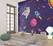Cosmic explorer wall mural with a cartoon astronaut, rocket ship, planets, and starry galaxy background in a playful kids’ playroom.