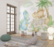 Cute dinosaur wall mural with watercolor-style dinosaurs, tropical plants, and soft pastel clouds, perfect for nurseries, kids' bedrooms, and playrooms.