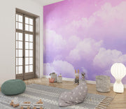 Dreamy cloud-themed wall mural with soft purple hues and fluffy white clouds, decorating a modern children's room with cosy accents, toys and a stylish rug.