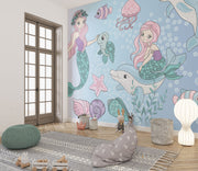 Whimsical underwater-themed mural with pastel mermaids, dolphins, turtles, jellyfish, and fish set against a blue bubble-filled background in a cozy kids' room.