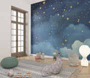 Starry night wall mural with golden stars and deep blue watercolor-style clouds, decorating a cozy playroom.