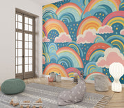 Bold and colorful rainbow wall mural with pink clouds and blue background, decorating kids playroom.