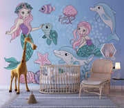 Whimsical underwater-themed mural with pastel mermaids, dolphins, turtles, jellyfish, and fish set against a blue bubble-filled background in a cozy kids' room.