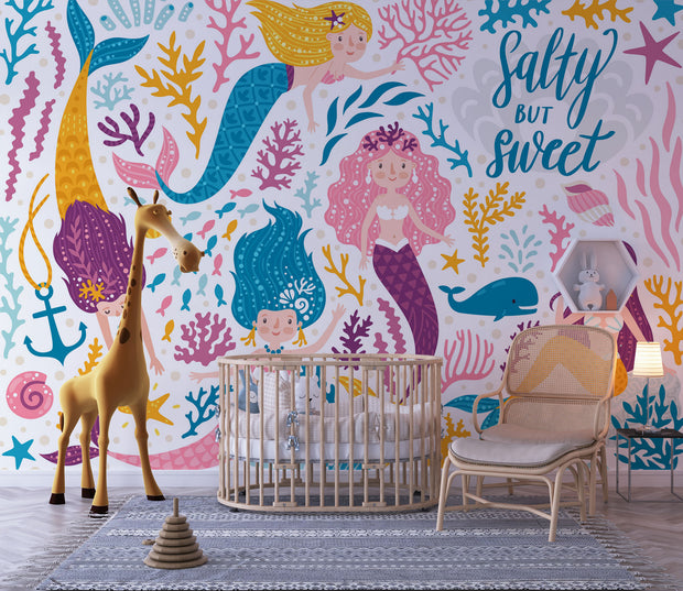 Colorful mermaid-themed wall mural in a children's playroom, featuring smiling cartoon mermaids with vibrant tails, sea creatures and coral.