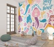 Colorful mermaid-themed wall mural in a children's playroom, featuring smiling cartoon mermaids with vibrant tails, sea creatures and coral.