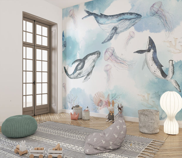 Underwater ocean wall mural with watercolor whales, jellyfish, and coral reefs in calming blue tones, displayed in a children's room with cozy decor.