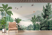 Scenic jungle wall mural with green tropical leaves, misty mountains, and flying cranes against a soft sunrise backdrop.