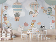 Nursery wall mural with pastel-colored forest animals flying in hot air balloons, surrounded by trees, clouds, and heart-shaped balloons