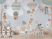 Nursery wall mural with pastel-colored forest animals flying in hot air balloons, surrounded by trees, clouds, and heart-shaped balloons